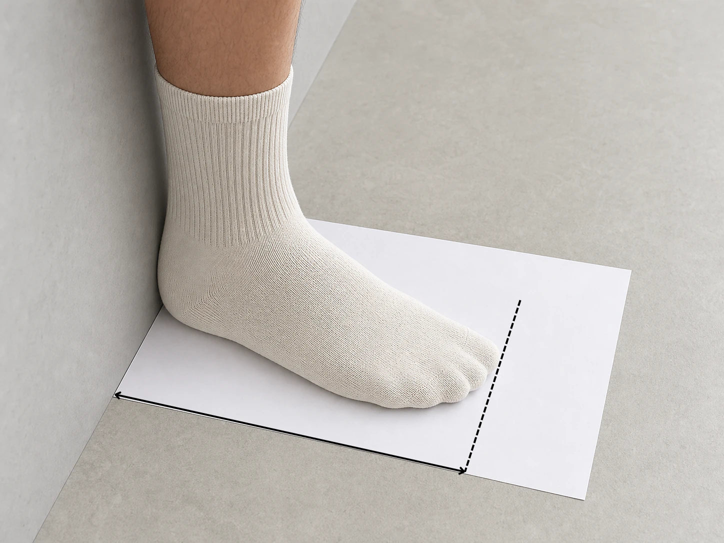 A socked foot standing on paper with the heel touching a wall